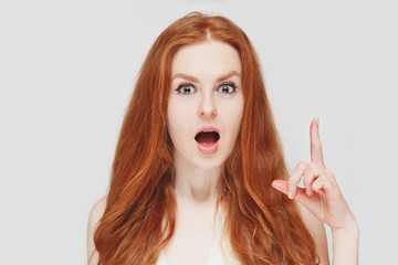 Beautiful redhead surprised woman picks up the finger. On white background. Expressive positive facial expressions.