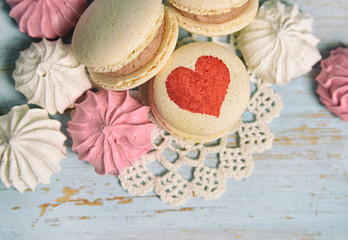 Fototapeta na wymiar Valentine's day or wedding sweets. Macaroons with heart shape and meringues on baby blue wooden background flat lay. Top view with copy space