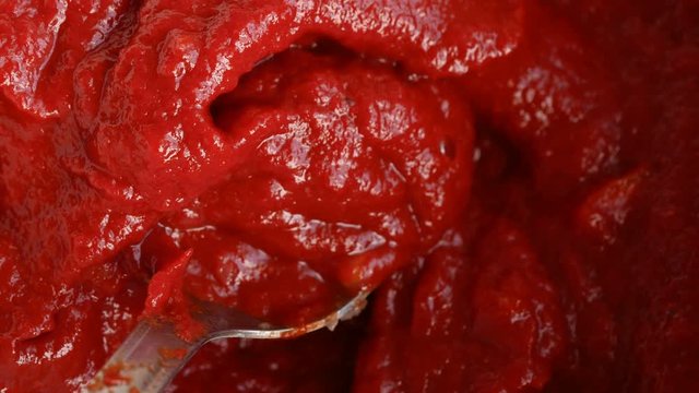 Macro of pouring salt on tomato puree and mixing it with spoon.