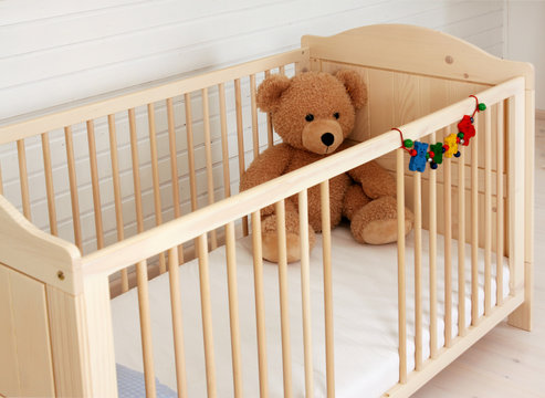 Ein Teddyb&auml;r sitzt in einem Kinderbett