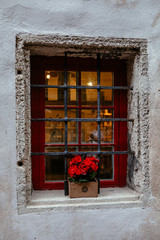 Fototapeta na wymiar Old stone house's window decorated with colorful petunia flowers in medieval old town of Tallinn, Estonia