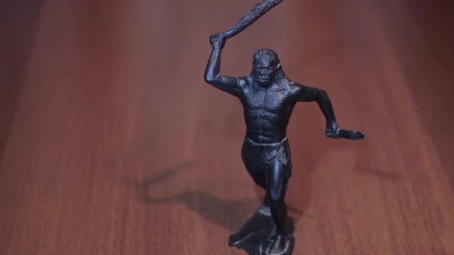 A caveman with a bat and knife in hands on dark background black toy