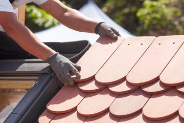 Hands of roofer laying tile on the roof. Installing natural red tile.