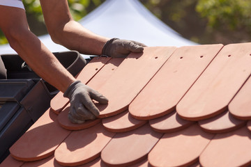 Hands of roofer laying tile on the roof. Installing natural red tile.