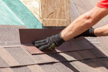 Roofer builder worker installing shingles on a new wooden roof with skylight © brizmaker