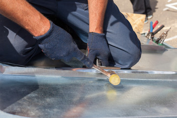 Roofer builder worker finishing folding a metal sheet using rubber mallet