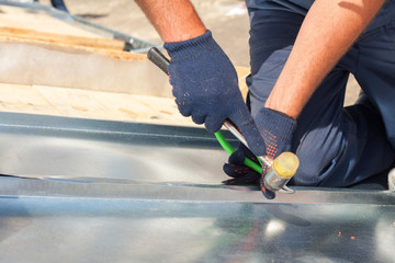 Roofer builder worker finishing folding a metal sheet using rubber mallet