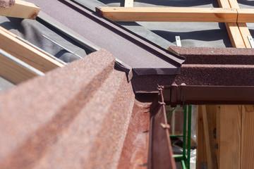 New asphalt shingle roof with brown rain gutter, wooden beams and vapour control layer