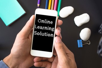 Online learning solution, text message on screen at hands take smartphone, black table with office supplies backdrop background . business concept.