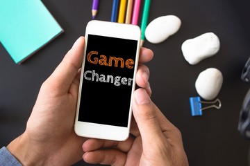 Game changer, text message on screen at hands take smartphone, black table with office supplies backdrop background . business concept. - obrazy, fototapety, plakaty