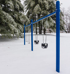 swings in playground  covered in ice and snow after winter storm 
