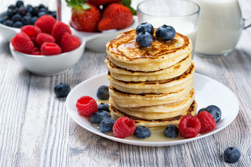 Stack of pancakes with fresh blueberry and raspberry, poured with honey. Milk and fresh berries, healthy breakfast concept