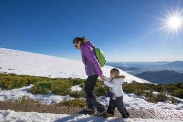 happy family winter scene of mother holding hands of three years old child hiking together in snow mountain summit of Navacerrada, in Madrid Spain
