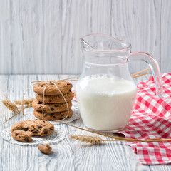Jug of milk and chocolate chip cookies on wooden background