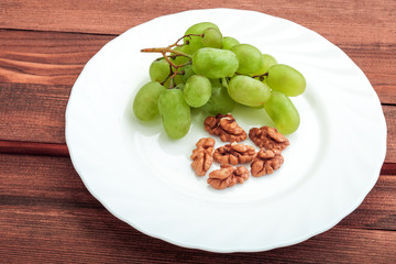 Green grapes and walnut in white plate on wooden table.