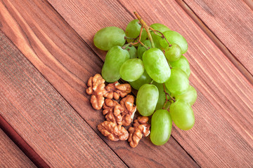 Green grapes and walnut on wooden table.