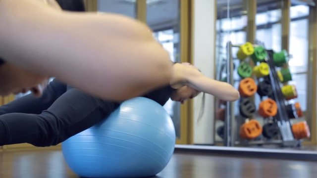 Female trainer in the gym doing hyperextension relying on fitball. Athlete lies on his stomach on a gymnastic ball, which is located on the pelvic region. Knees bent legs apart at shoulder width
