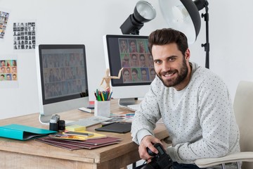 Happy photographer holding camera at his desk
