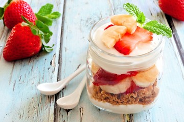 Healthy strawberry and banana parfait in a mason jar on a rustic blue wood background