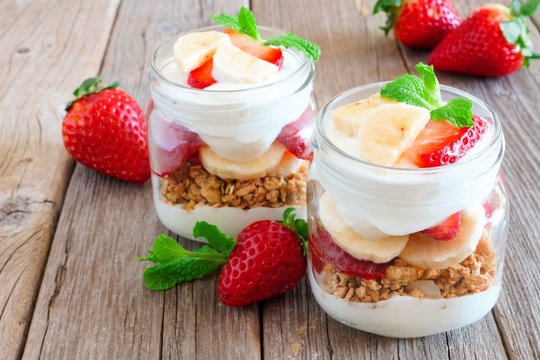Healthy strawberry and banana parfaits in mason jars on a rustic wood background