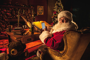 Santa holds a smartphone at his desk with Christmas decor in the background