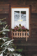 Window on a wooden building facade decorated with flowers and covered with snow.
