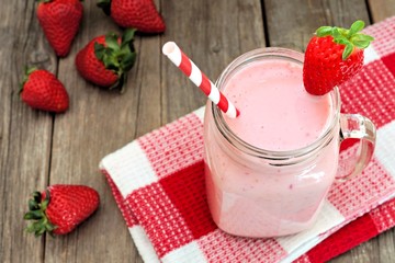 Healthy strawberry smoothie in mason a jar mug with checkered cloth against rustic wood