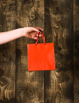 red orange shopping bag in female hand on wooden background