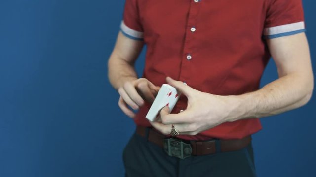 Close up magician in red shirt perform playing cards magic tricks. Blue background