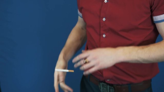 Close up illusionist in red polo shirt telekinesis magic focus cigarette fly in to his mouth. Blue background