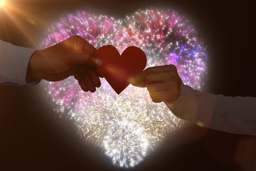 Composite image of couple holding paper heart shape paper