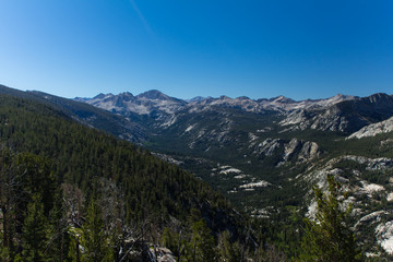 Rounded granite mountains and dense forests surround a high altitude valley in the high sierra in summer