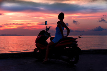 A woman sitting on a motorcycle, enjoy the evening sunset and the sea.