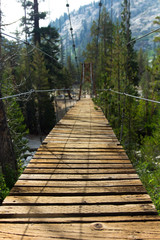 An old wooden suspension bridge with broken slats hangs over a river near the Rae Lakes in California's high sierra