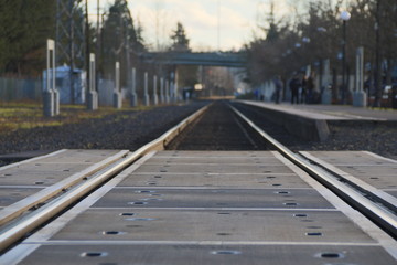 Close Up of Railroad Tracks/Crossing with Passengers, Platform, Trees in Blurred Blurry Soft-Focus in Background, Cutting Edge, Daytime - Oregon