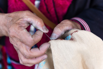 old lady's hand making a cross stitching pattern 