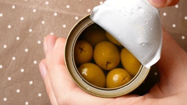 Top view of hand opening olive tin can and taking out olives.