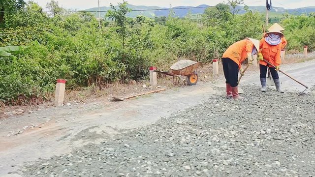 DA LAT, LAM DONG/VIETNAM - SEPTEMBER 02 2016: Camera moves past people in special uniform laying asphalt on country road against landscape in Vietnam
 on September 02 in Da Lat