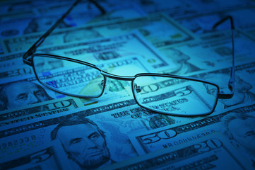 Naklejka premium Glasses on dollar money, blue tone, Business financial concept