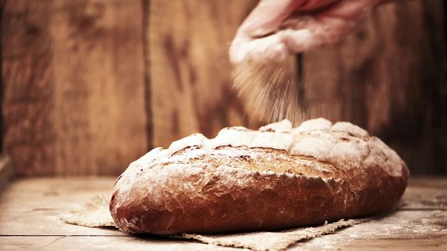 Slow motion of chef hands pouring flour on homemade bread.