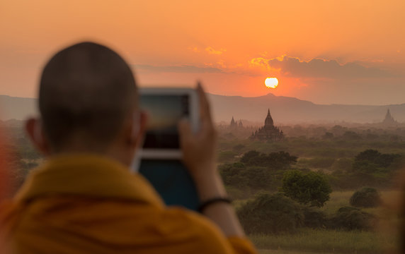 Buddhist monk travel and take a photos of beautiful sunset over the ancient temple in Bagan plains of Myanmar.