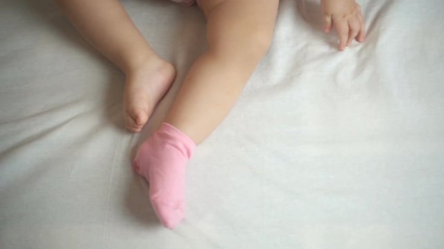 Mother puts pink socks on baby's legs, slow motion, top view hd video