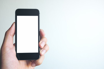 Mockup image of hand holding black mobile phone with blank white screen on white background room