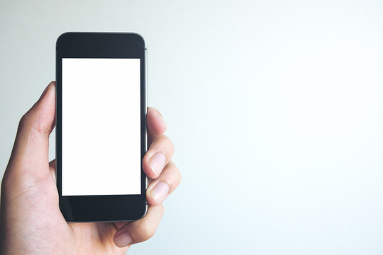 Mockup image of hand holding black mobile phone with blank white screen on white background room