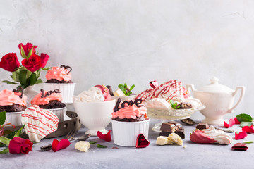 Beautiful chocolate cupcake, pink cream, meringue cookies and red roses on gray stone background. Valentines, Mother Day, wedding concept with copy space.