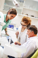 Obraz premium Dentist and her female assistant in dental office talking with senior patient and preparing for treatment.|Examining x-ray image.