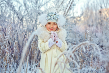 Happy adorable child girl in fur hat and coat in winter forest