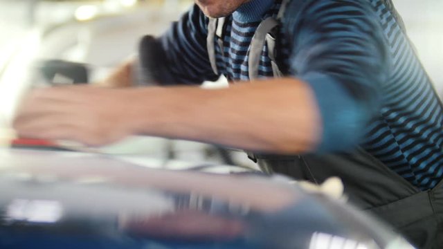 Automobile service - a worker polishes a blue car, back light
