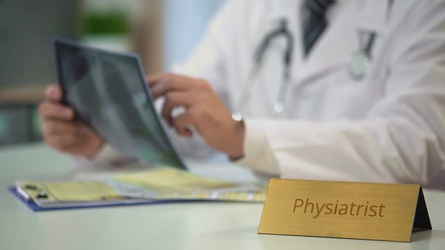 Male physiatrist analyzing x-ray image and prescribing treatment, health care