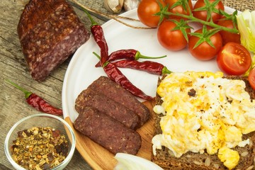 Scrambled eggs with bread and salami. Egg breakfast on a wooden table. Healthy food.